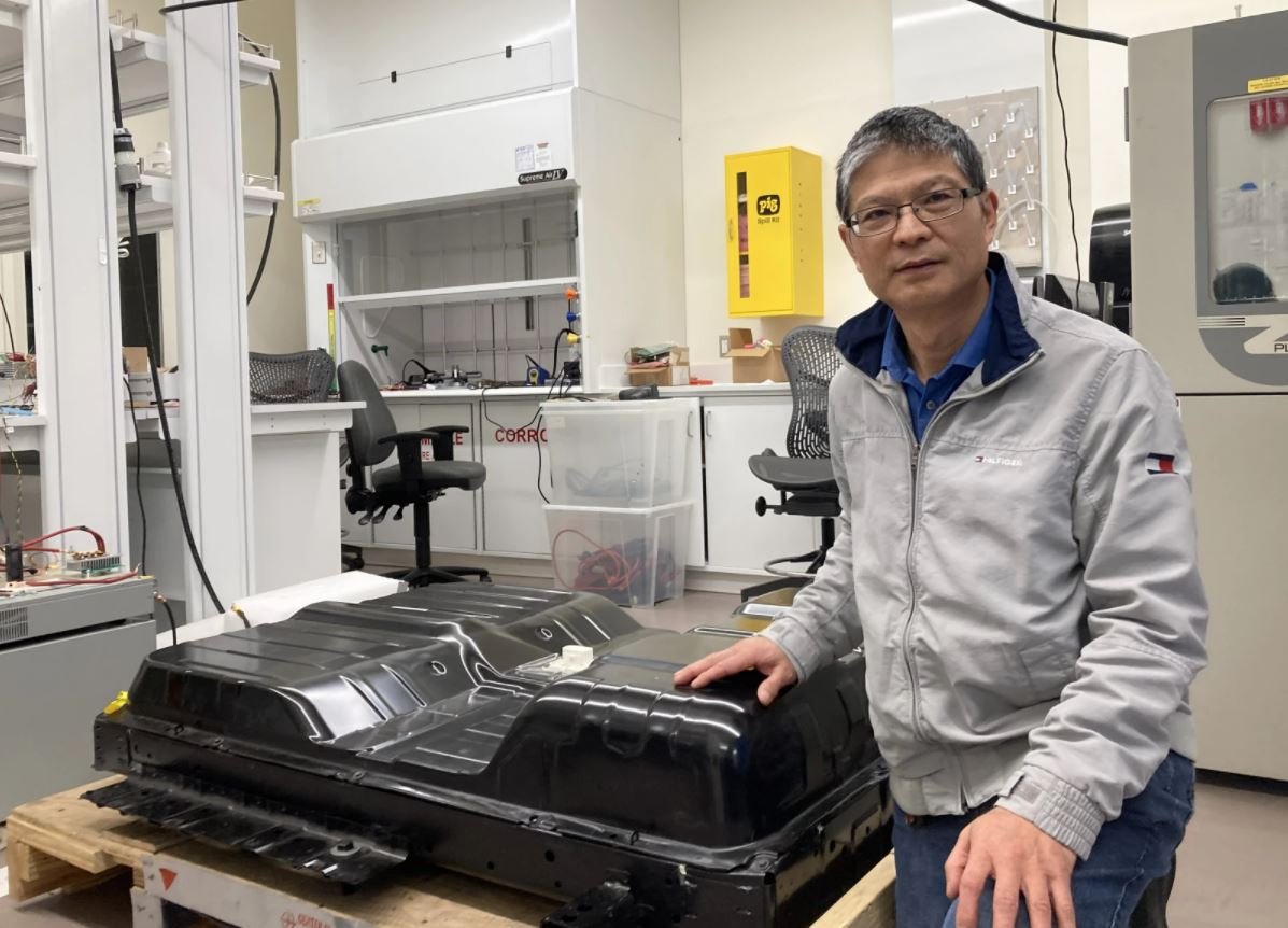 Engineering professor Chris Mi kneels next to a used electric vehicle battery in his lab at San Diego State.