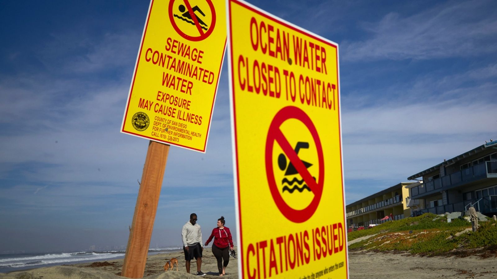 AP Photo/Gregory Bull In this Dec. 12, 2018, file photo, a couple walk along the beach as signs warn of contaminated water at Imperial Beach, Calif.