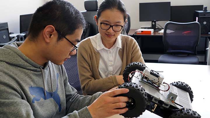 Dr. Junfei Xie and a student work on a robotic vehicle project in a lab setting.